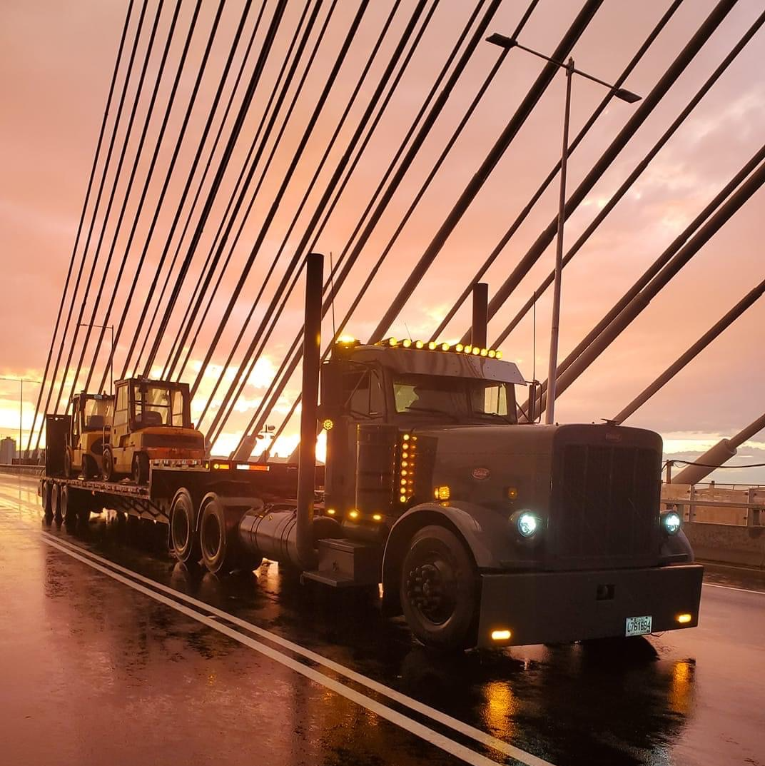 Camion TLM & Fils transportant des engins de chantier sur un pont au coucher du soleil